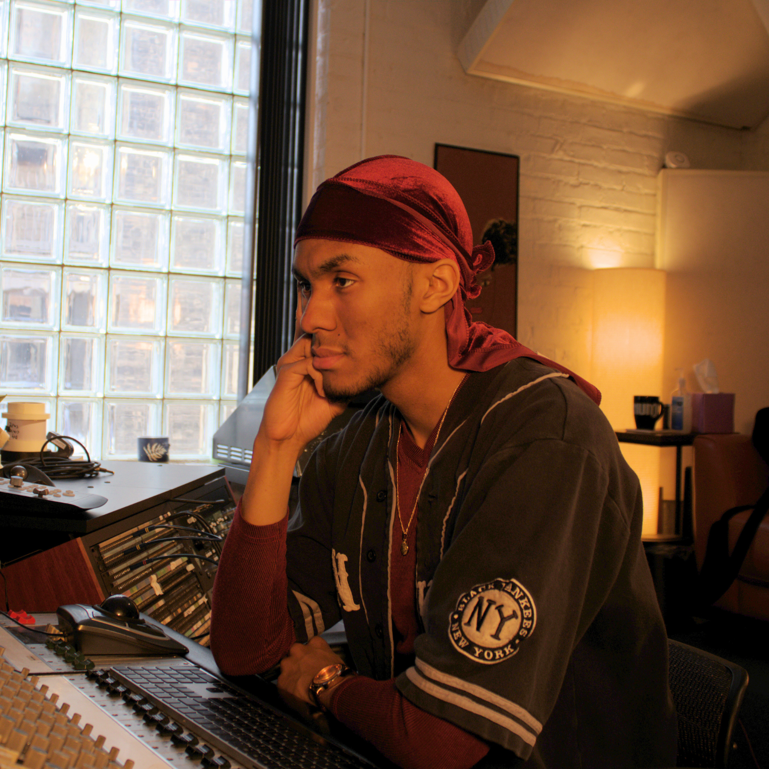 music producer sitting at recording console with red durag and black jersey